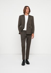 Brown double-breasted suit jacket with two front pockets, paired with matching slim-fit trousers, and a white crew-neck T-shirt. Black shoes.