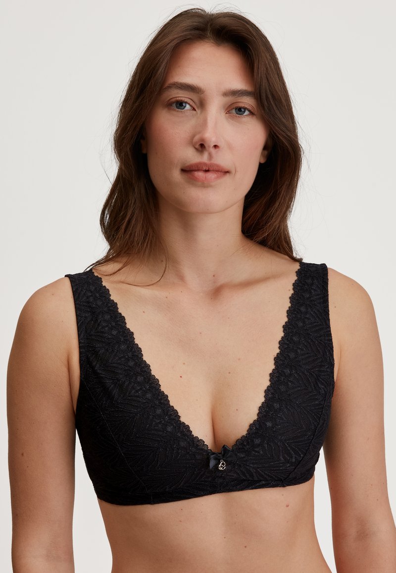 Zwarte kanten bralette met een diepe V-hals, een gestructureerd bladerenpatroon, brede banden en een klein strikje in het midden voor.