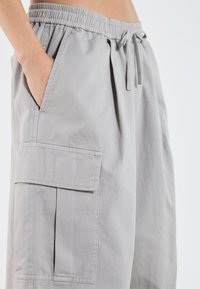 Shorts cargo gris clair en tissu lisse, dotés d'une taille élastique avec cordon de serrage, de poches latérales et d'une grande poche cargo sur le côté.