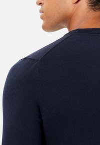 Granatowy sweter dzianinowy o prążkowanej strukturze, z okrągłym dekoltem i detalami na szwie ramion, pokazany z boku i z tyłu.