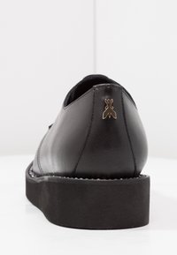 Scarpa in pelle nera con una finitura liscia, punta rotonda e suola piattaformata. Presenta un piccolo emblema dorato sul tallone.