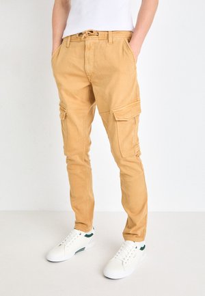 Pantalones cargo beige con bolsillos laterales, cintura ajustable y un corte ajustado. Combinados con zapatillas blancas con detalles verdes.