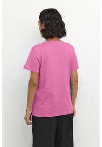 T-shirt en coton fuchsia à manches courtes, avec un col rond et une texture lisse, montrée de dos sur un mannequin contre un fond uni.