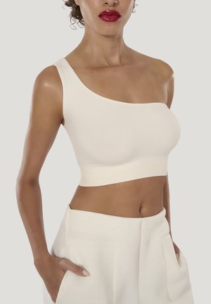 Asymmetrisk krämfärgad bralette i mjukt tyg, med en bred axelband på ena sidan och ett slätt band, kombinerad med matchande byxor.