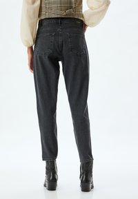 Hoge taille, zwarte denimspijkerbroek met een relaxte pasvorm, voorzien van twee achterzakken en een recht model, gecombineerd met zwarte enkellaarsjes.