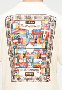 Πίσω μέρος μπλουζάκι με γραφικό γηπέδου ποδοσφαίρου FIFA Παγκόσμιο Κύπελλο USA 94, φθαρμένο, με πολλαπλές εθνικές σημαίες και ονόματα ομάδων γύρω από το περίγραμμα.