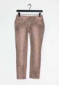 Béžové džíny s úzkým střihem. Disponují pěti kapsami, pěti knoflíky a jemnými texturovými variacemi. Zavěšeny na černém ramínku.