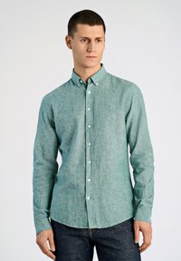 Ljus turkos, knappad skjorta med krage, lång ärm och textilstruktur. Har vita knappar och en rundad nederkant. Bärs med mörka jeans.