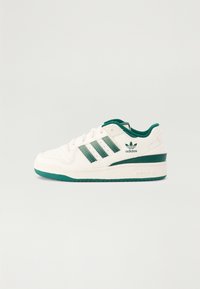 Bijela tenisica s zelenim detaljima, koja sadrži tri zelene pruge, perforirani prednji deo, podstavljen ovratnik i gumeni potplat.