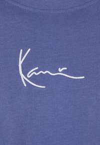Blue cotton t-shirt featuring a white embroidered signature design. The fabric is smooth with a round neckline and short sleeves.