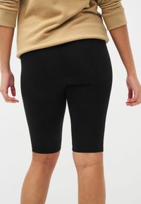 Leggings noirs arrivant aux genoux, fabriqués en tissu extensible, avec une texture lisse et une taille élastique. Aucun motif ni matériel visible.
