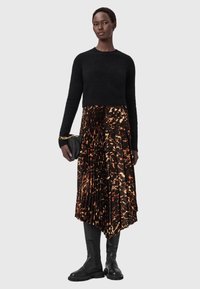 Mustat lyhytcroppaustakki, laskostettu midi-hame, jossa oranssia ja ruskeaa abstraktia kuviota, polviin ulottuvat mustat saappaat ja pieni musta clutch-laukku.