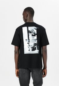 Black cotton t-shirt featuring a large monochrome graphic on the back, with short sleeves and a relaxed fit.