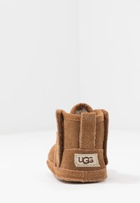Ruskean mokkanahkaiset nilkkurit, joissa on pehmeä pinta. Niissä on UGG-logopatch ja pyöristetty kärki. Näkyvät ompeleet ja ylellinen vuori.