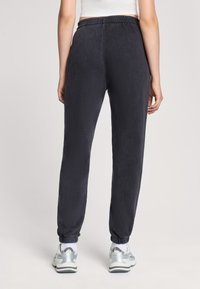 Ciemnoszare dresy z elastycznym pasem, zwężane nogawki i elastyczne mankiety przy kostkach, noszone z srebrnymi butami sportowymi.