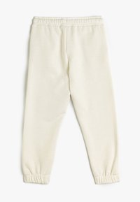 Cremefarvede sweatpants lavet af blødt stof. Har elastisk talje og snøre ved anklerne. Glat tekstur, enkelt design.