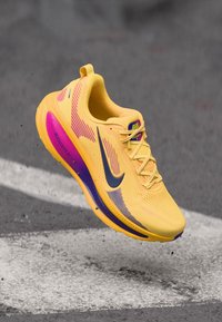 Κίτρινο παπούτσι για τρέξιμο με μωβ λεπτομέρειες, διαθέτει πλέγμα στο επάνω μέρος, υφή στη σόλα και μαύρο λογότυπο Swoosh. Τα κορδόνια είναι ανοιχτό κίτρινα, η μεσαία σόλα είναι μαλακή και απορροφητική.