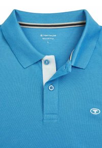 Polo shirt blu con tessuto testurizzato, dotato di colletto bianco, patta con tre bottoni e un piccolo logo sul lato sinistro del petto.