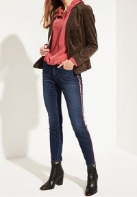 Ruskea corduroy-takki, vaaleanpunainen huppari, tummat farkut, joissa vaaleanpunainen sivuraita, ja mustat nilkkurit. Sileät pinnat ja istuva malli.