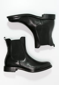 Botas de tobillo de cuero negro con paneles laterales elásticos, punta redondeada, tacón robusto y lengüetas para ponerlas y quitarlas con facilidad. Suela plana con textura antideslizante.