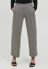 Pantalon large à motifs vichy noir et blanc avec poches latérales, taille haute et texture lisse. Porté avec des sandales plates noires.