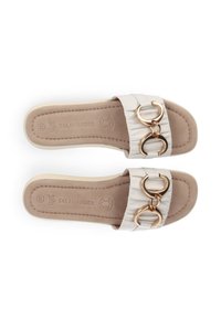 Weiße Rutschsandalen mit strukturierten Riemen, ausgestattet mit zwei goldenen runden Akzenten. Weiches beiges Fußbett mit geprägt Logo der Marke, flaches Sohlen-Design.