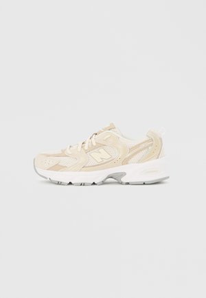 Beżowo-biały sneaker New Balance 530 z siateczkową i zamszową cholewką, białymi sznurowadłami, amortyzowaną podeszwą ABZORB oraz logo "N" po boku.