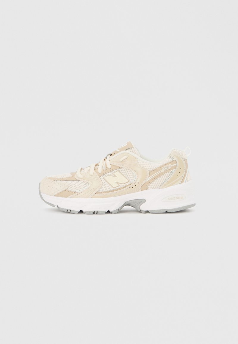 Bēša un balta New Balance 530 sneaker ar sietveida un zamšāda virsmu, baltiem šņorēm, ABZORB polsterētu zolīti un "N" logotipu sānos.