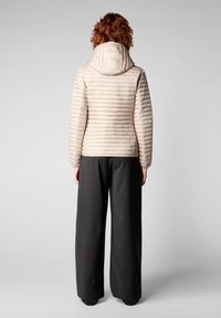 Doudoune beige clair avec capuche, présentant des coutures horizontales et une coupe ajustée. Associée à un pantalon large noir.