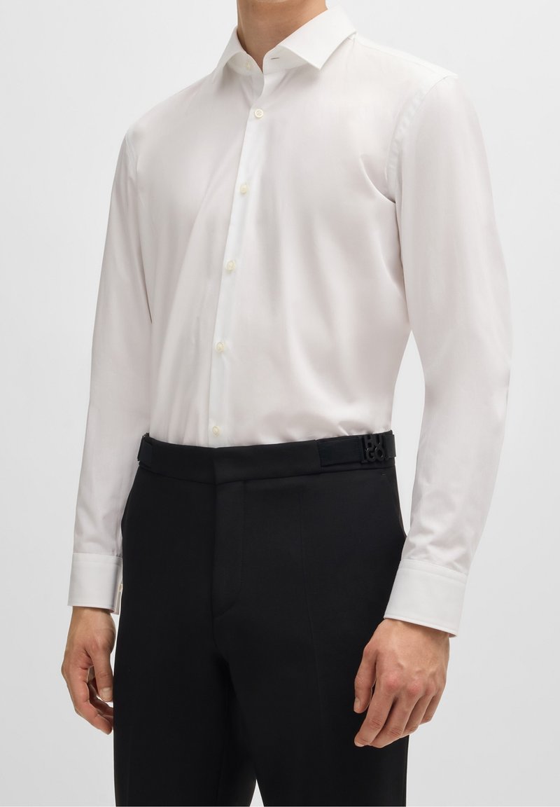 Biała koszula z długim rękawem, klasycznym kołnierzem, dopasowanym krojem i zapinana na guziki z przodu, zestawiona z czarnymi, szytymi na miarę spodniami oraz designerskim paskiem.