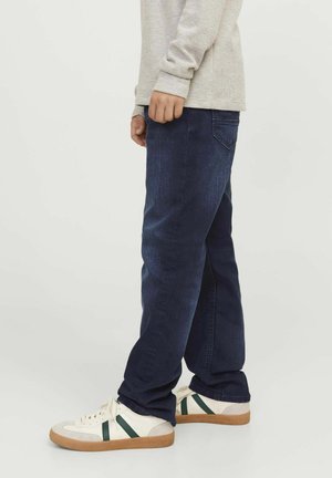 Tumesinised denim püksid sirge lõikega, selga pandud heleda halli pikaga särgi ja beežide spordijalatsitega, millel on rohelised triibud. Lihtne disain, ilma nähtavate mustriteta.