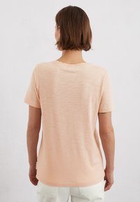 Light peach, short-sleeve t-shirt with a relaxed fit. Soft, textured fabric with a round neckline and a small tag on the left side.