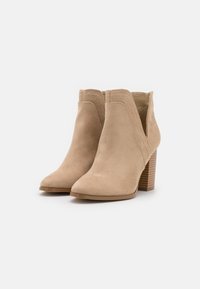 Beige Wildleder-Stiefeletten mit spitzem Zeh, ausgeschnittenen Seiten und strukturiertem Blockabsatz. Nähte auf dem Obermaterial sorgen für visuelles Interesse.