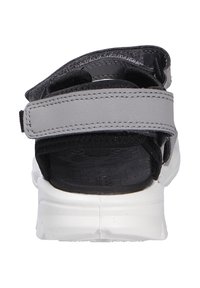 Grå sandal med en sort tekstureret rem og justerbar Velcro-lukning. Har en hvid sål med udtalt mønster for godt greb.