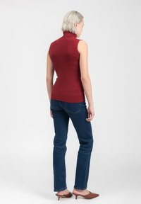 Top rosso senza maniche con colletto alto abbinato a jeans blu scuro. Il top presenta una texture a coste e un design aderente, completato da mule con tacco marroni.
