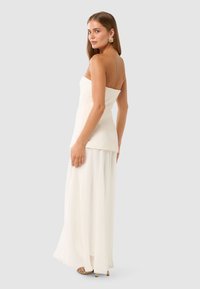 Weißes trägerloses Kleid mit einem taillierten Oberteil und fließendem Rock, das eine glatte Textur aufweist. Minimalistisches Design mit subtiler Eleganz und ohne Muster.
