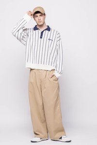 Sudadera blanca a rayas con cuello azul y logo, combinada con pantalones de pierna ancha beige. La modelo lleva una gorra beige y zapatos blancos.