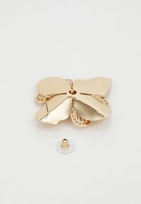 Broche en or en forme de fleur avec quatre pièces en métal poli en forme de pétale et des détails intérieurs texturés ; inclus une épingle de fixation amovible.