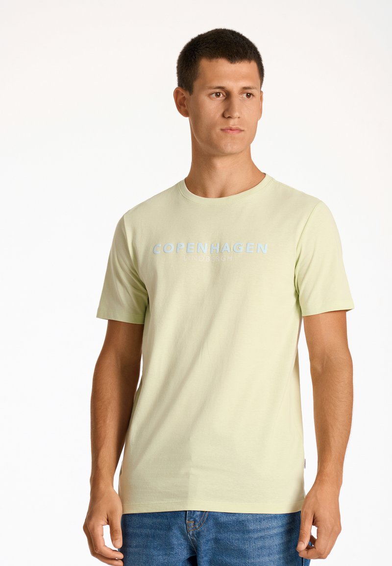 Camiseta de algodón verde claro con cuello redondo y mangas cortas. "COPENHAGUE LINDENBERGH" impreso en azul pálido en el pecho.