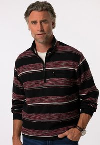 Czarny pulower na zamek błyskawiczny z poziomymi czerwonymi, białymi i szarymi paskami. Posiada długie rękawy i kieszeń na piersi. Wykonany z miękkiego materiału dzianinowego.