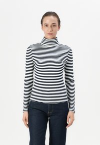Cămașă cu guler înalt cu dungi alb-negru, cu m�âneci lungi, textură canelată și un logo mic pe piept, asortată cu blugi din denim de culoare bleu închis.
