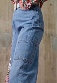 Calças cargo de denim azul claro com um corte solto, apresentando um grande bolso lateral e detalhes de costura discretos.