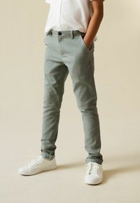 Chinos verde chiaro con vestibilità slim e tasche laterali, dotati di chiusura con bottone. Abbinati a sneaker bianche, ideali per un look casual.