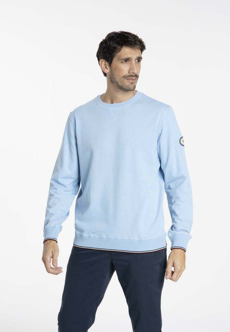 Sweatshirt bleu clair à manches longues, avec des poignets et un ourlet côtelés, et une petite logo cousue sur la manche gauche. Texture lisse, coupe décontractée.