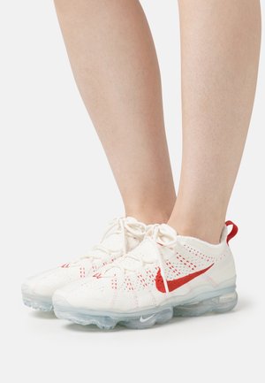 Bílá teniska s červenými akcenty, strukturou pleteného svršku, šněrováním a průhlednou vzduchovou podrážkou. Na boku je výrazné logo Swoosh.