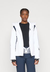 Balta nepralaidi striukė su gobtuvu, užtrauktuku priekyje ir tamsiai mėlynomis detalėmis. Sujungta su juoda ilgomis rankovėmis palaidine ir tamsiai mėlynomis kelnėmis. Lygus paviršius.