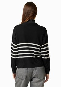 Maglione a righe bianche e nere con orlo a costine, dotato di maniche lunghe e vestibilità rilassata, indossato su jeans grigi.