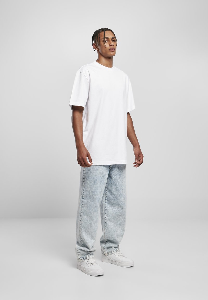 Biely oversized tričko, svetlo modré acid-wash džínsy a biele tenisky. Krátke rukávy, voľný strih a jednoduchý dizajn.