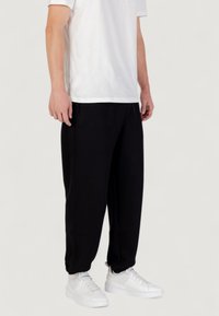 Zwarte joggingbroek met een relaxte pasvorm, voorzien van elastische boorden en zijzakken, gecombineerd met witte sneakers en een eenvoudig wit T-shirt.