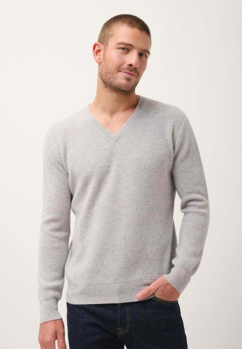 Suéter gris claro de cuello en v con textura acanalada, mangas largas y un diseño ajustado, combinado con jeans azul oscuro. Un look simple y sobrio.